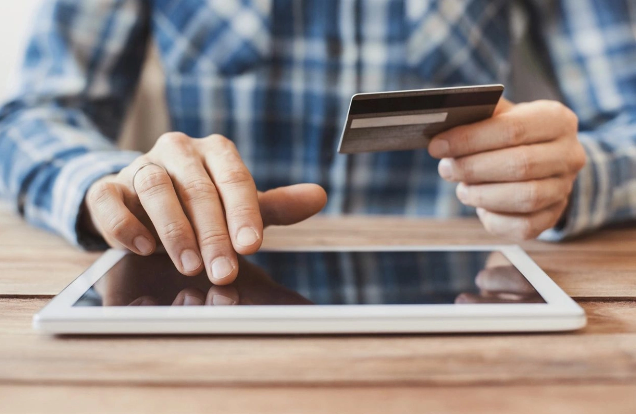 A person holding a credit card and using a tablet.