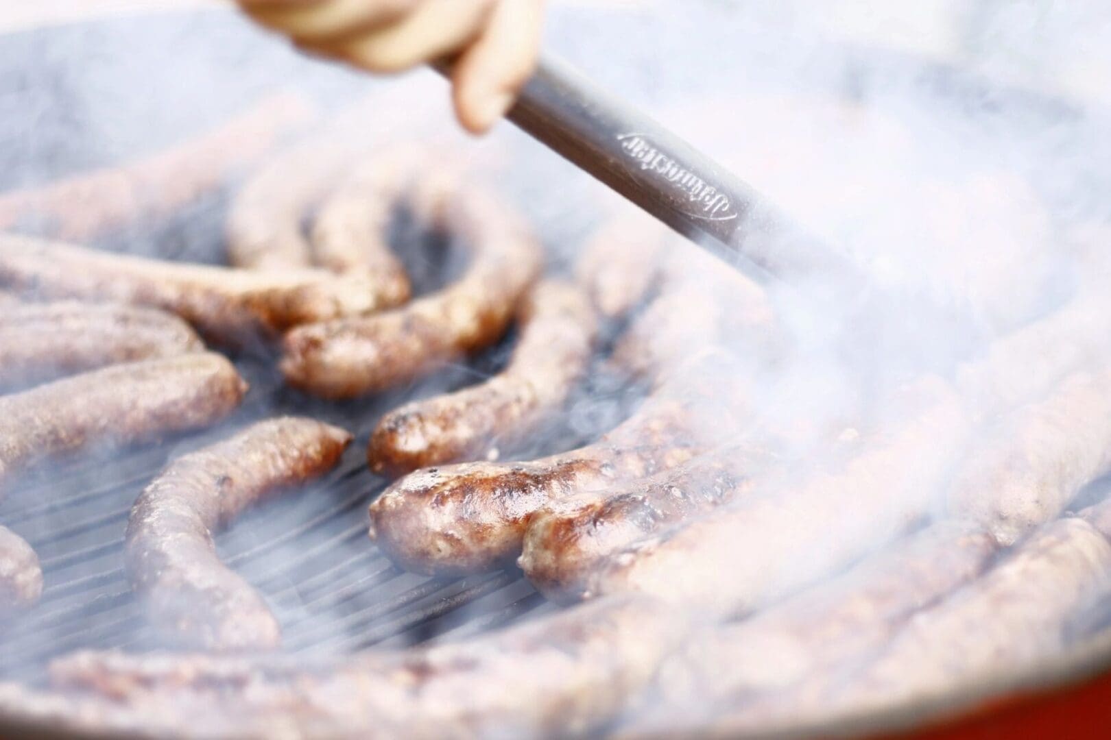 A person is cooking sausage on an outdoor grill.